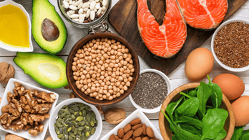 Avocado, salmon, nuts, and legumes on a table representing foods rich in healthy, fatty acids.