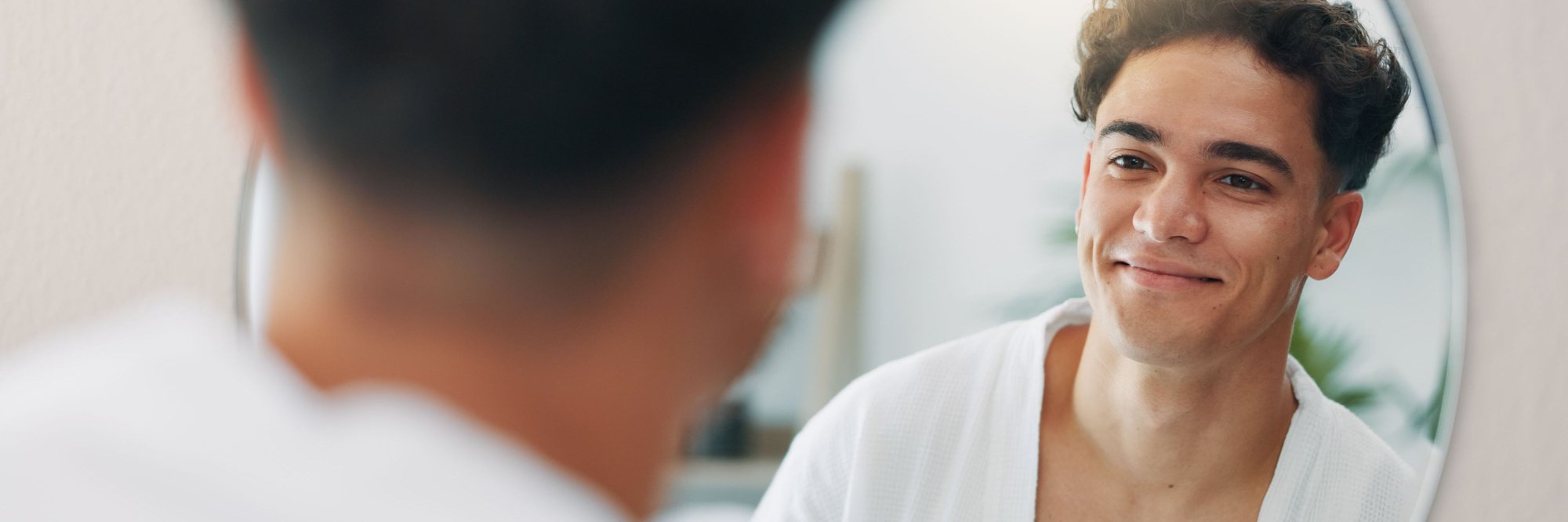 Young man looking in a mirror with clear skin recently treated by DermatologistOnCall