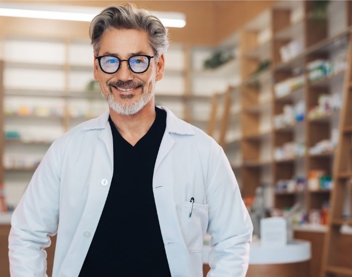 Middle-aged, male pharmacist standing in front of shelving.